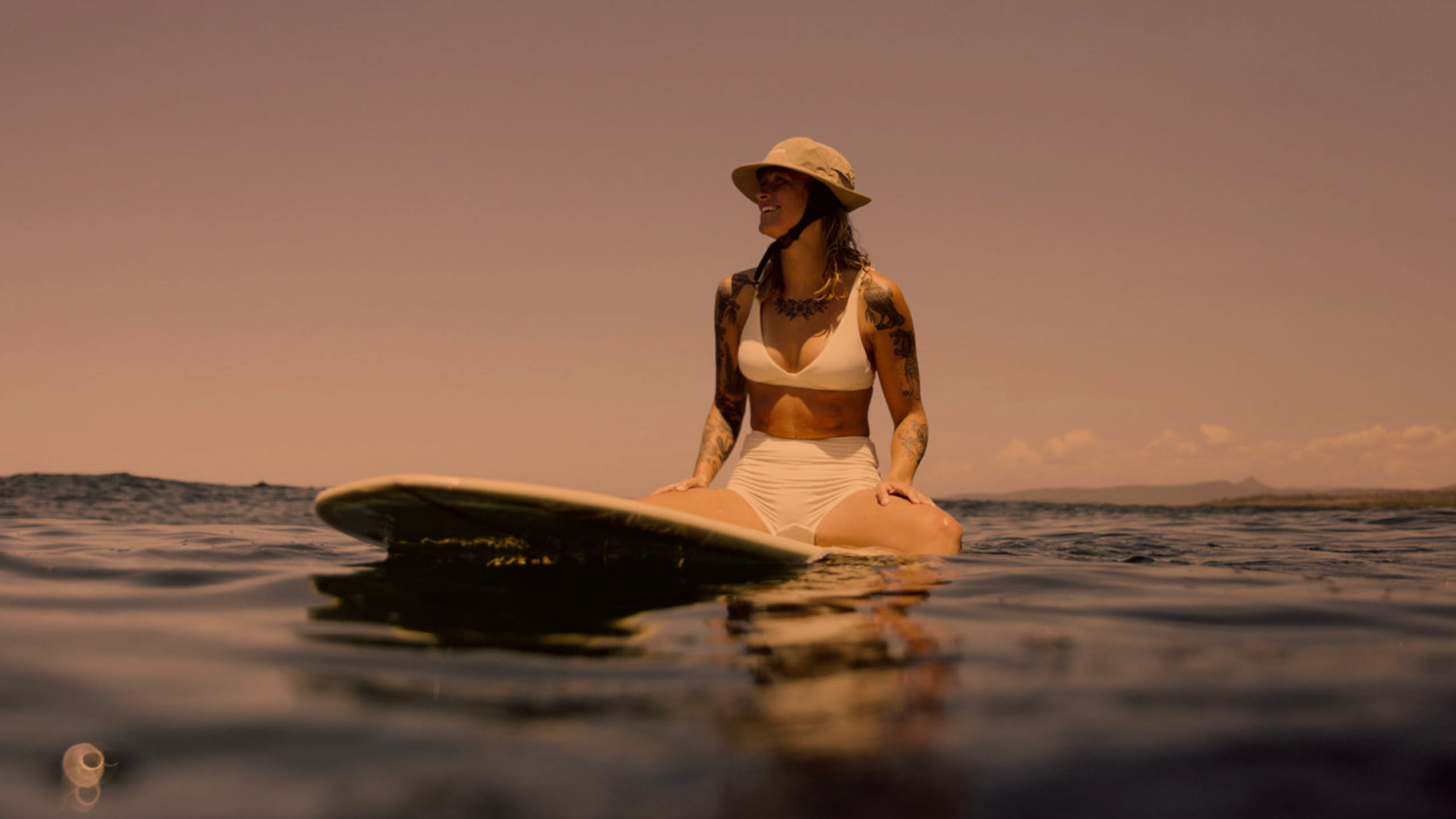 Girl in a surf bikini waiting for a wave. Longboard. Surf Hat. Smile. Nice ocean weather.