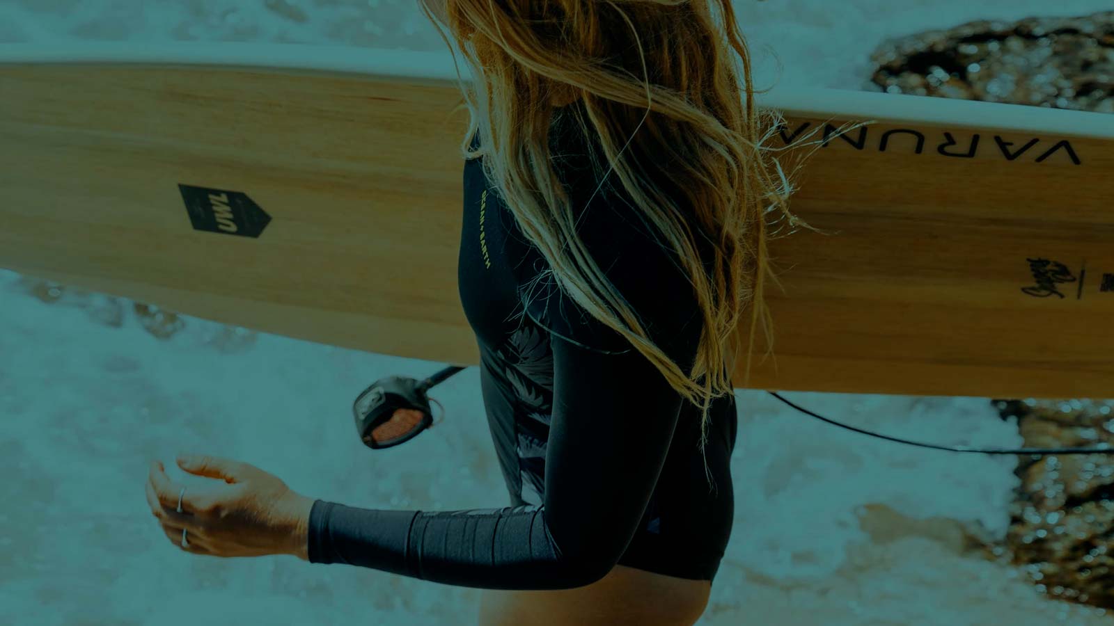 Girls with wet blond hair standing in white water with surfboard in her hand ready to paddle in.