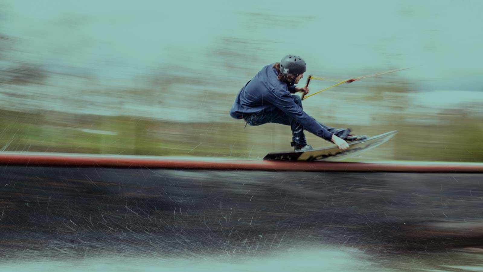 Wakeboarding riding over a rail with good speed. Top Layer jacket protecting him from wind chill and water splashes.