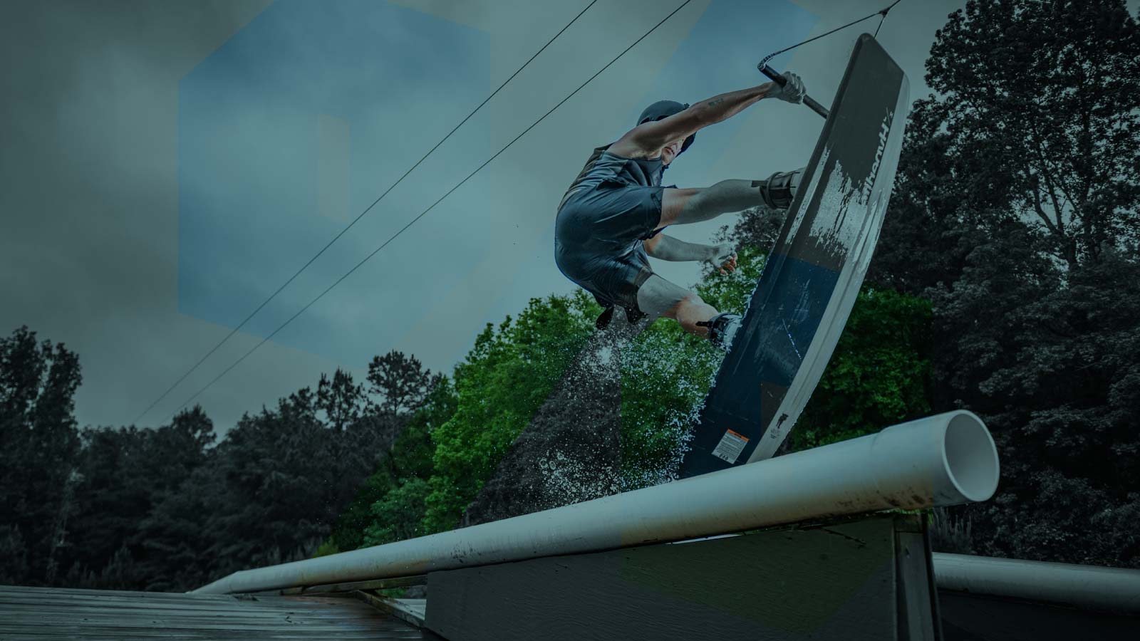 Wakeboarder tailpresing over a pipe in two tower cable park. Used and demo wakeboarding equipment at reduced prices — boards, bindings, vests, and other gear that still have plenty of life left in them.Used and demo wakeboarding equipment.