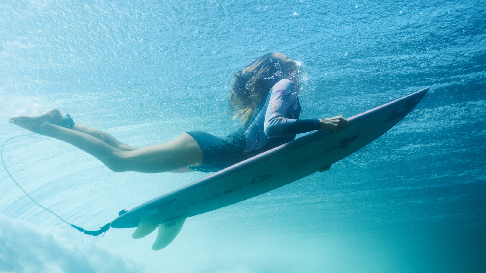Women's Short Wetsuits. Girl duckdiving trough the wave with a surfboard.
