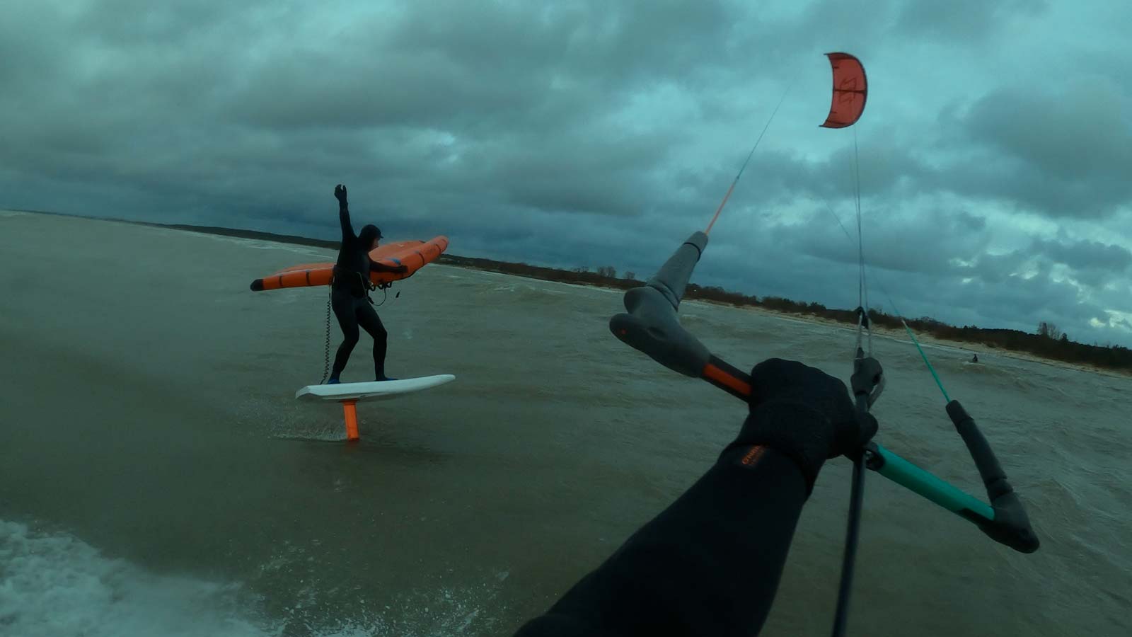 Kitesurfer stearing a kite and capturing wing rider catching a wave. Cold water session. Wetsuits.