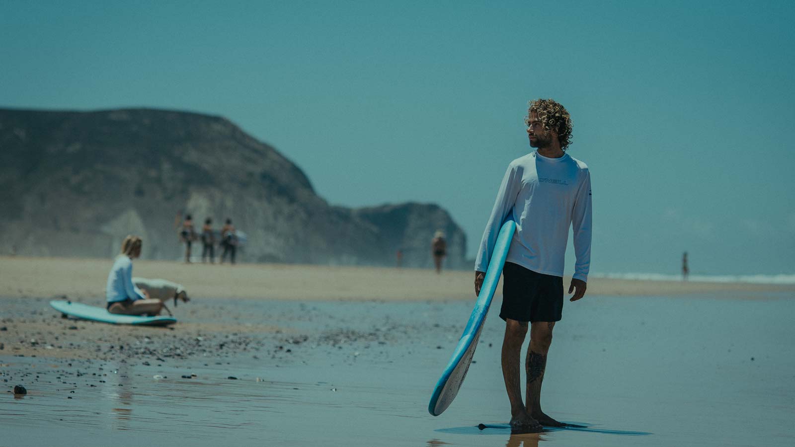 Surfer standing in the beach with surfboard in his hand an thinking about girl he just passed.O'Neill Men's Sunshirts and Tops for watersports and beach leisure.