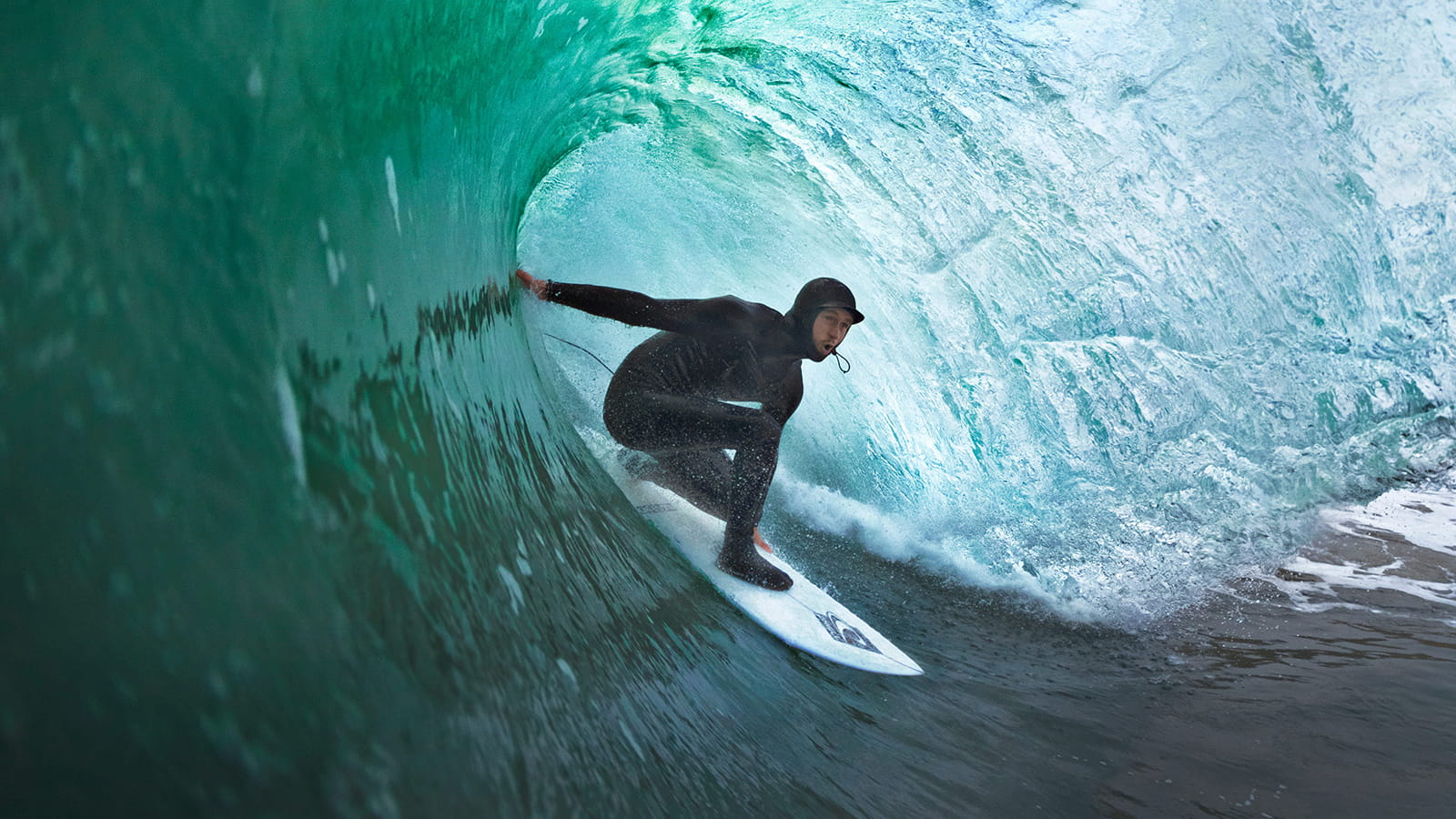 Neoprene Hoods | Surfer getting barreled in the massive tube. Turquoise clear water.