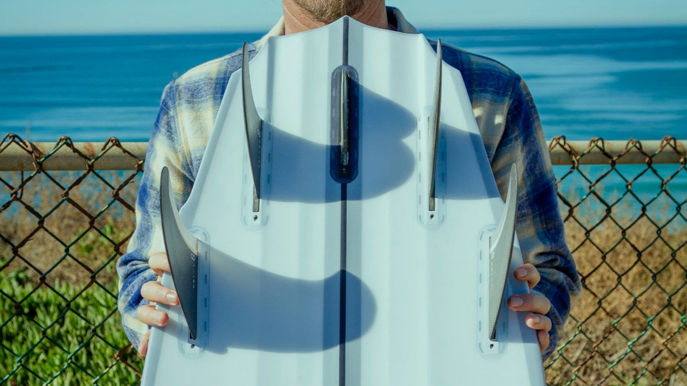 Male holding ion to hands brand new surfboard. Closeup pictures with surfboard tail and Quad fins.