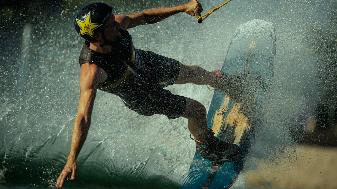 Athlete male wakeboarding truough the water. Wakeboard tail glide. handle with rope. Water splash.