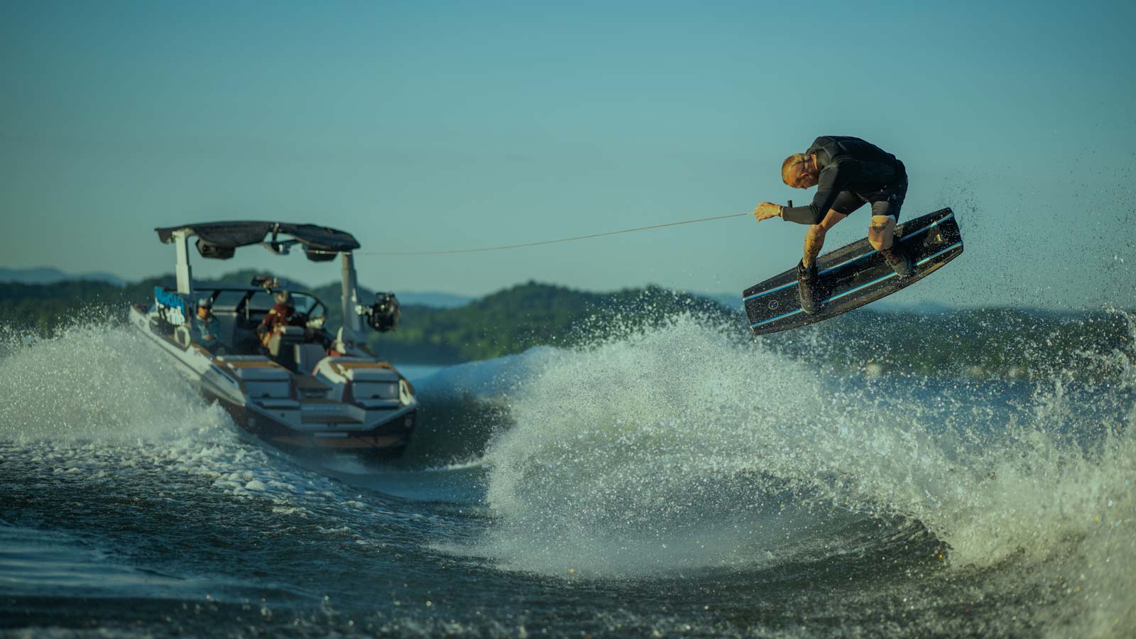 Wakeboarder jumping off the wake getting pulled by the boat.