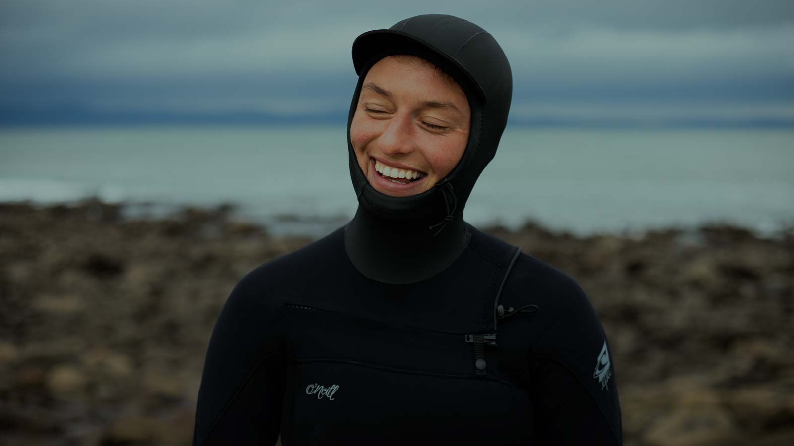 Girl smiling wearing hooded wetsuit.