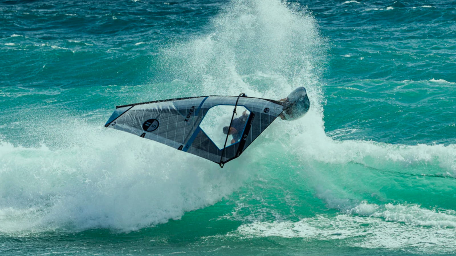 Windsurfer jumping with spray from turqouse blue ocean wave.